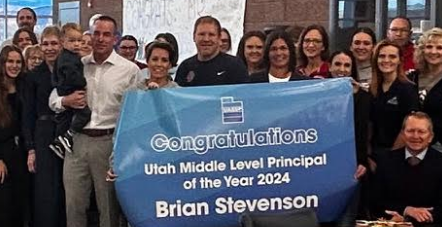 A group of students and teachers stand behind a banner announcing Brian Stevenson as the Utah Middle Level Principal of the Year.